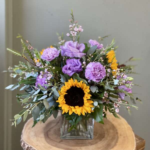 Sunflower and purple floral arrangement in a square glass vase