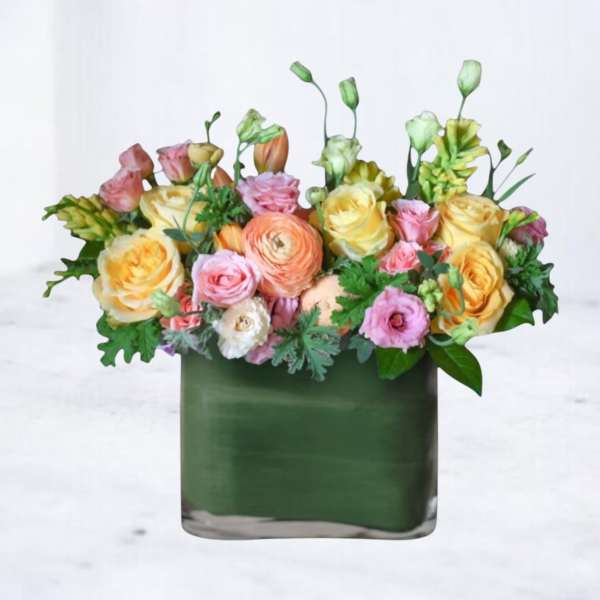Low arrangement of yellow roses and pastel ranunculus in a green rectangular vase