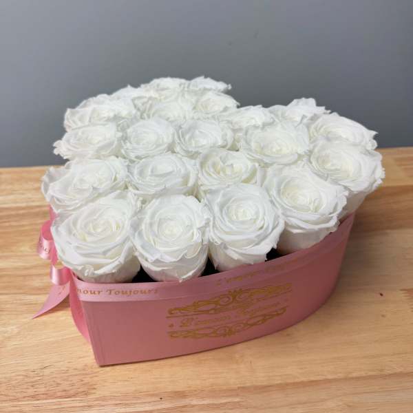 Heart-shaped pink box filled with tightly packed white roses on a wooden surface