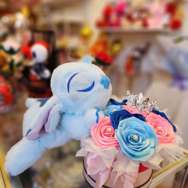 Plush bunny beside a box of blue and pink roses with a small crown