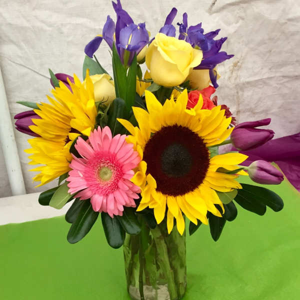 Colorful bouquet with sunflowers, roses, irises, and a gerbera daisy in a glass vase