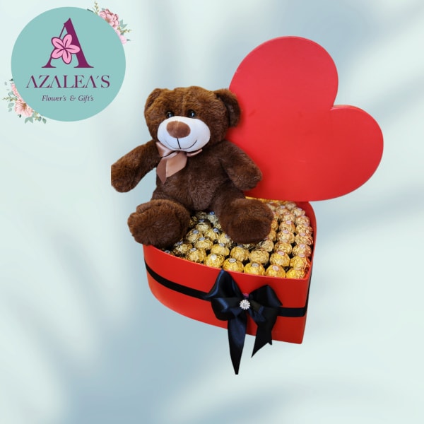 Teddy bear sitting in a red heart-shaped box filled with chocolates