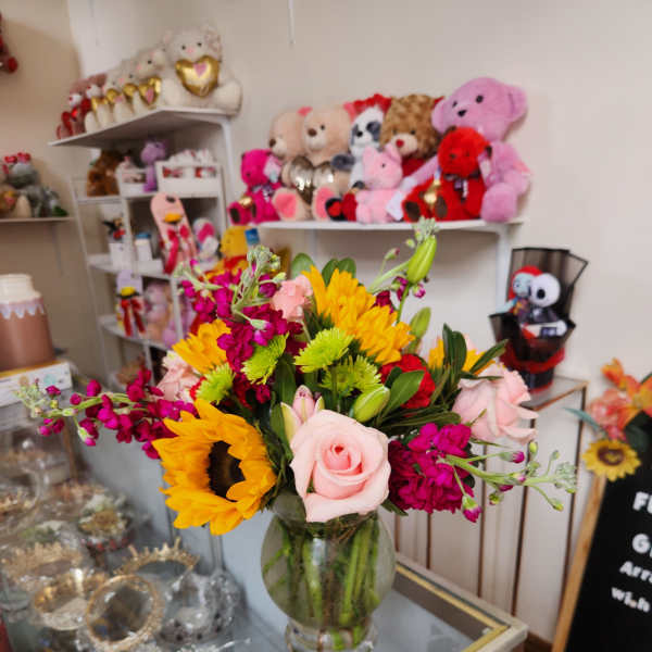 Mixed bouquet with sunflowers, pink roses, and magenta blooms in a glass vase