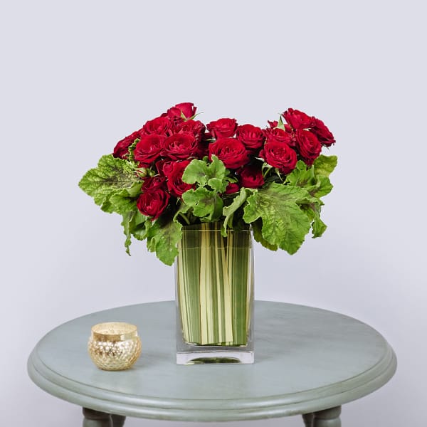 Red roses in a tall glass vase with a small gold candle holder