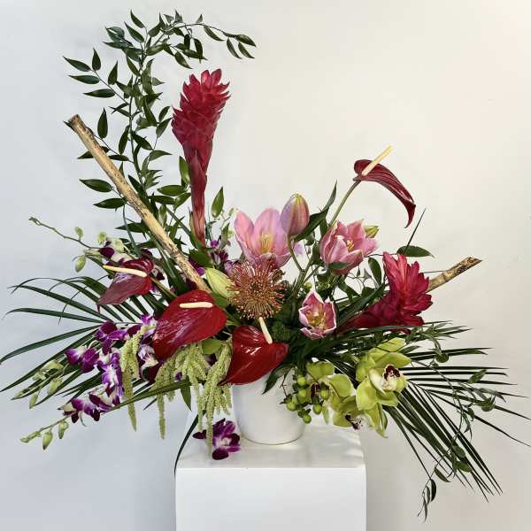 Tropical floral arrangement with red anthuriums, pink lilies, and orchids in a white vase