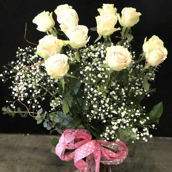 Bouquet of pale yellow roses with baby's breath in a glass vase and pink ribbon