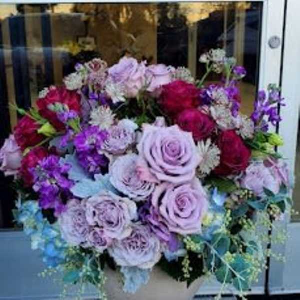 Round arrangement of lavender and red roses with purple blooms in a light ceramic bowl