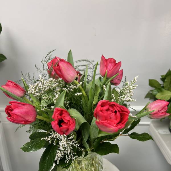 Vase of bright pink tulips with white filler flowers arranged in a textured glass vase