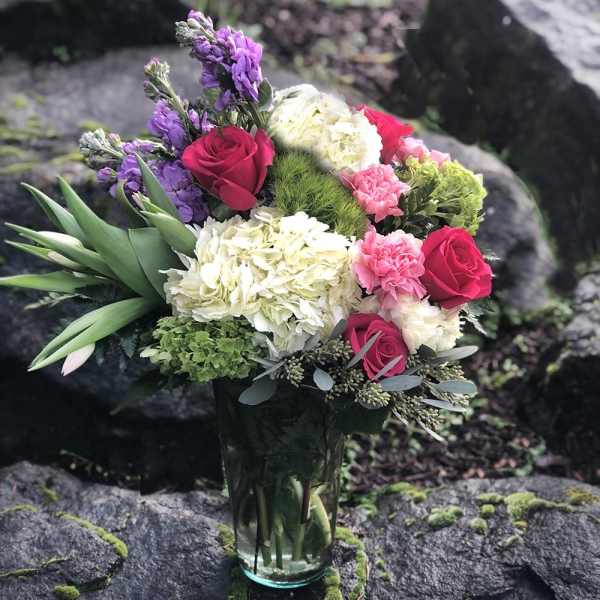 Bouquet of roses, hydrangeas, and purple flowers in a glass vase