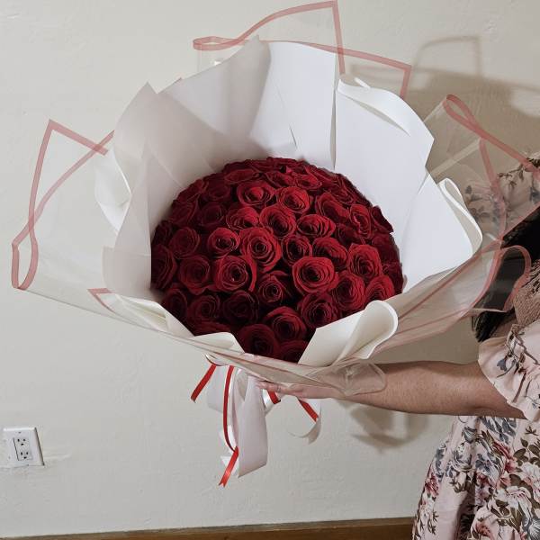 Large bouquet of red roses wrapped in white paper with pink ribbon