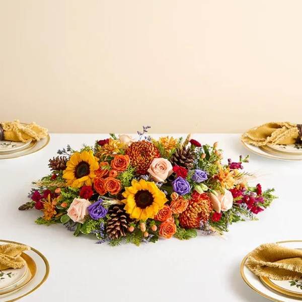 Low floral centerpiece with sunflowers, roses, and autumn blooms on a table