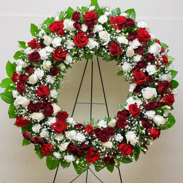 Standing circular wreath of red and white roses and white carnations on a metal easel