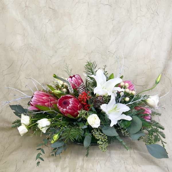 Low floral arrangement with pink protea and white lilies in a shallow container
