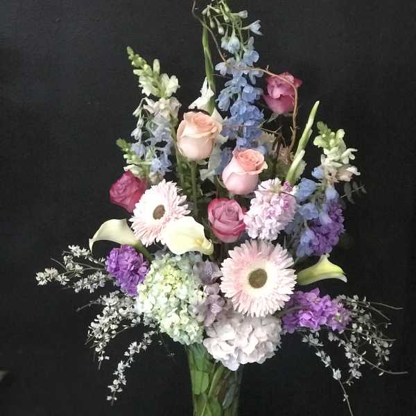 Tall mixed bouquet in a glass vase with pink roses and pastel blooms