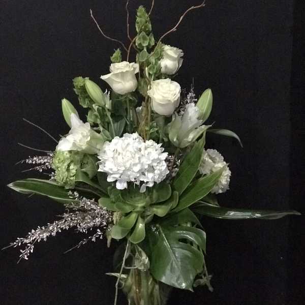 White floral arrangement with roses, lilies, and hydrangea in a tall vase