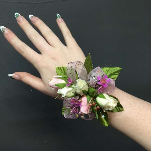 Wrist corsage with small white and pink roses and purple accents on a person’s arm