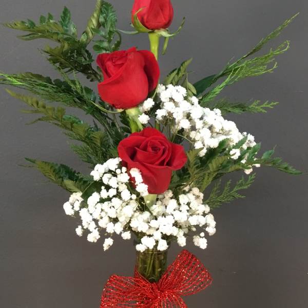 Three red roses in a clear vase with white baby's breath and a red bow