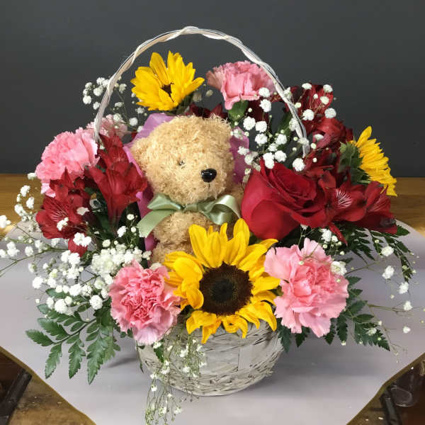 Basket arrangement with a teddy bear, sunflowers, roses, and pink carnations