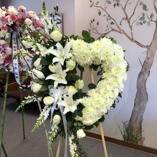 White floral funeral wreath on a wooden stand with ribbon.