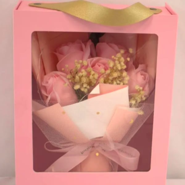 Pink boxed bouquet of pink roses and small yellow filler flowers wrapped in tulle with ribbon