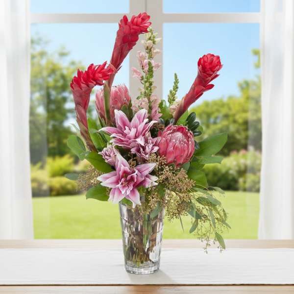 Tall pink lilies and protea with red tropical blooms in a clear glass vase