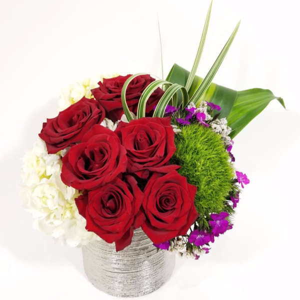 Red roses arranged in a silver vase with white and purple accents