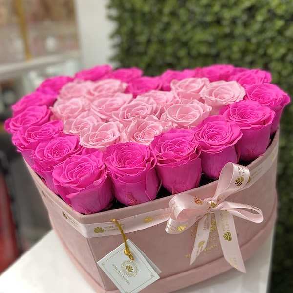 Heart-shaped box of bright and light pink roses with ribbon and tag