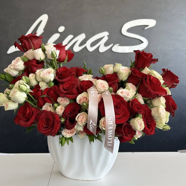 Red and blush roses arranged in a white vase with ribbon