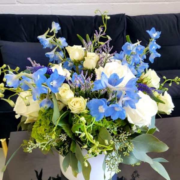 Blue and white flower arrangement with roses and delphinium in a white vase on a black table