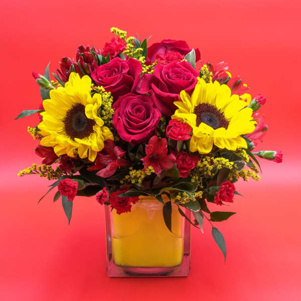 Bouquet of red roses and yellow sunflowers in a square glass vase