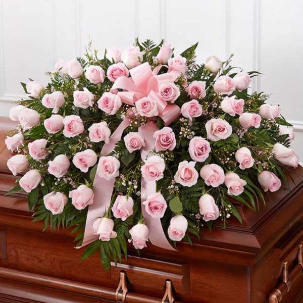 Large spray of light pink roses with ribbon displayed on a wooden casket.