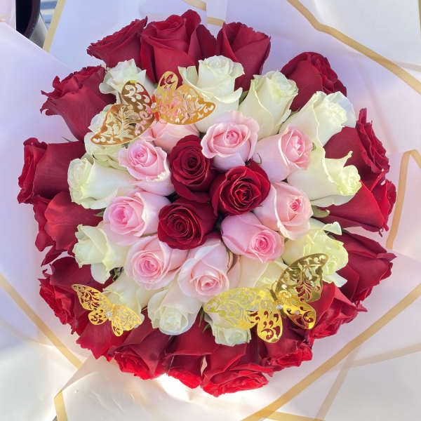 Bouquet of red, pink, and white roses wrapped in white paper with gold trim