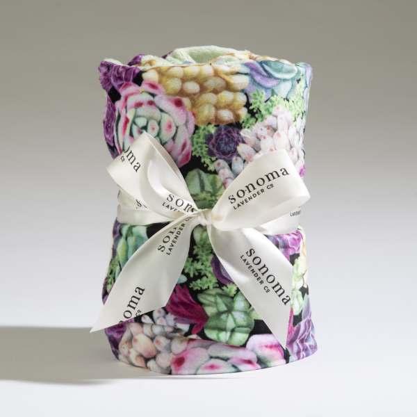 Rolled plush blanket with colorful succulent print tied with a white logo ribbon