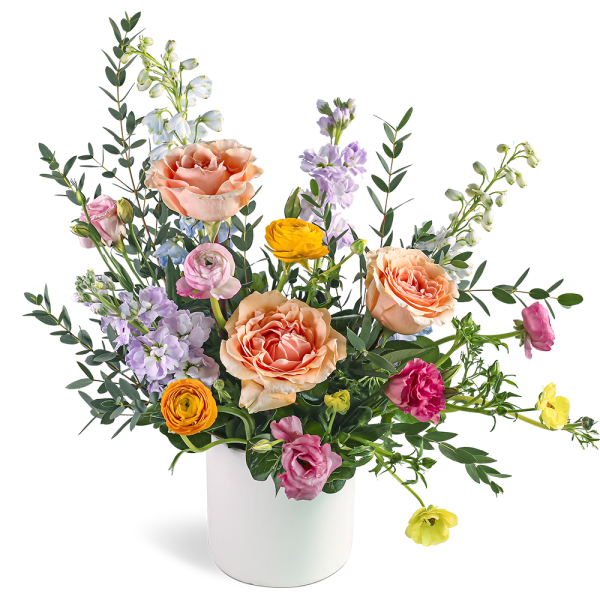 Peach roses and colorful ranunculus with pastel blooms in a white cylinder vase