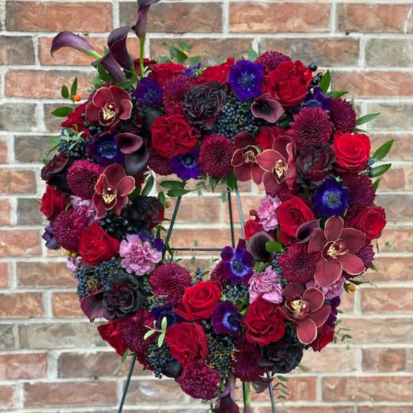 Heart-shaped floral wreath with red, purple, and black blooms on a stand