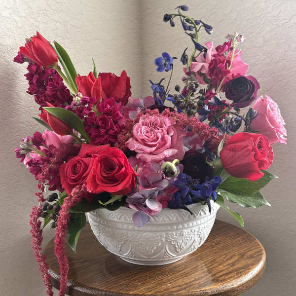 Mixed bouquet of red, pink, and blue flowers in a white bowl vase