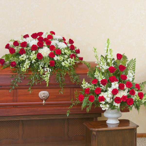 Red and white funeral floral set with casket spray, standing wreath, and tall urn arrangement