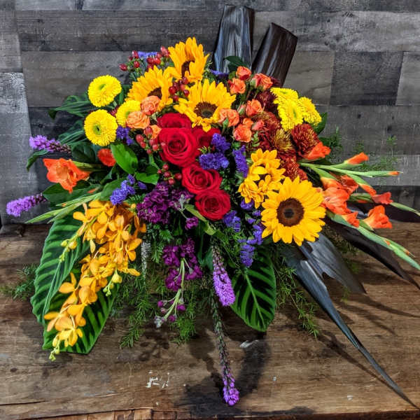 Vibrant horizontal arrangement with sunflowers, red roses, orchids and mixed flowers on a rustic wooden surface