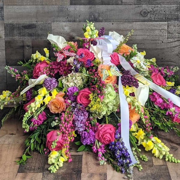 Bright mixed casket spray with pink roses, yellow snapdragons, hydrangeas, and white ribbons.