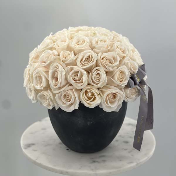 Cream rose bouquet in a black vase with a gray ribbon