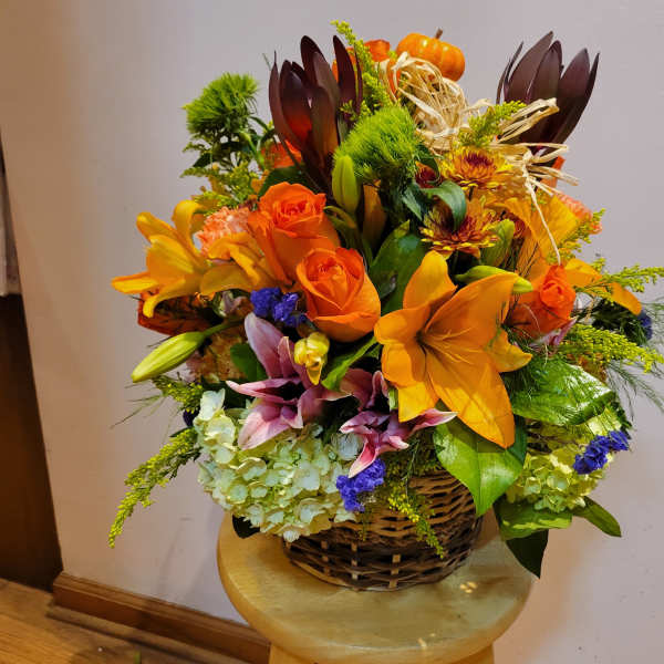 Basket arrangement with orange lilies, roses, and autumn accents