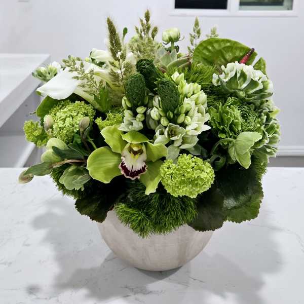 Green floral arrangement in a round white vase with white and lime blooms