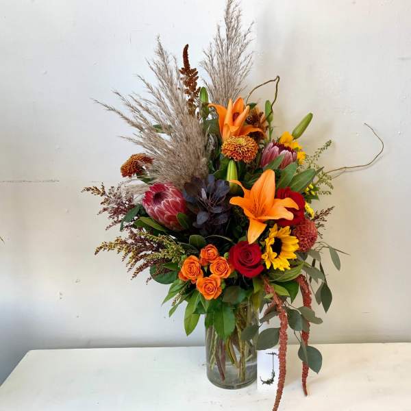 Tall mixed bouquet with orange lilies, red roses, and sunflowers in a glass vase