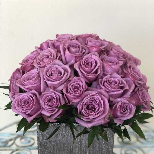 Lavender rose arrangement in a gray textured square vase on a decorative metal table
