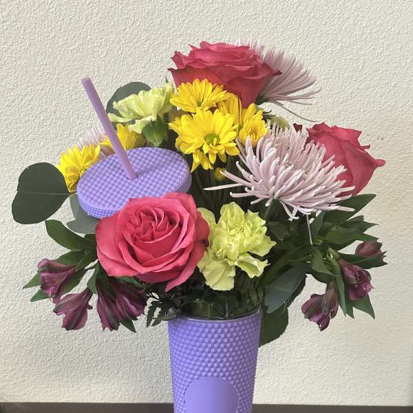 Bright mixed bouquet with pink roses and yellow daisies in a tall lavender tumbler cup with straw