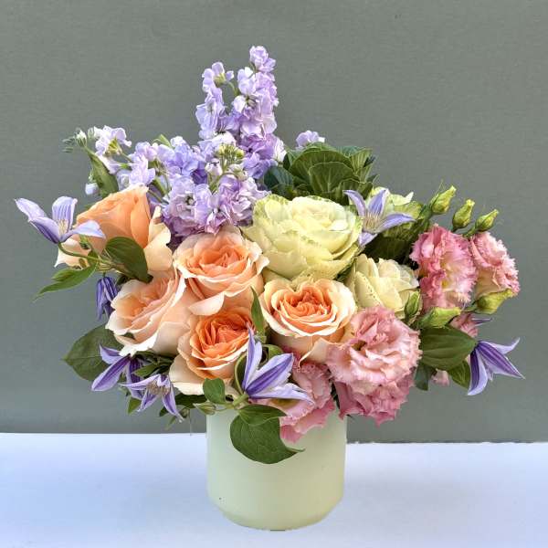 Pastel bouquet of roses, lisianthus, and purple blooms in a pale vase