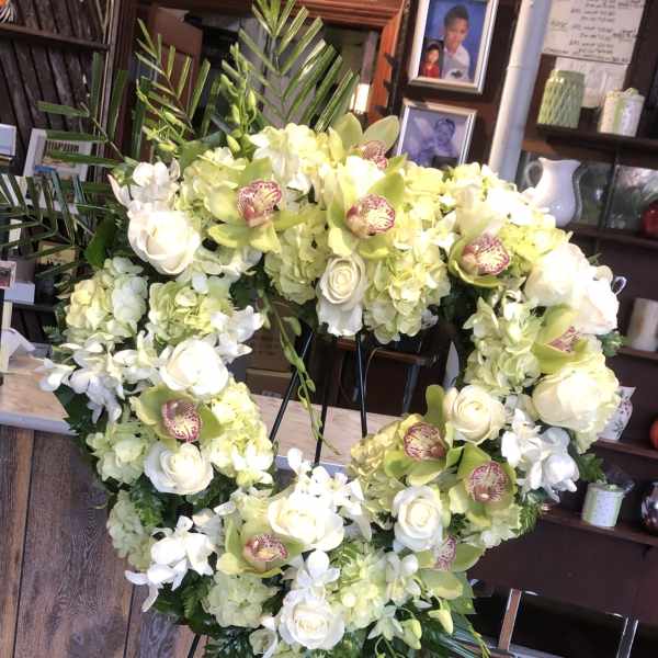Heart-shaped floral wreath with white roses and pale green orchids on an easel