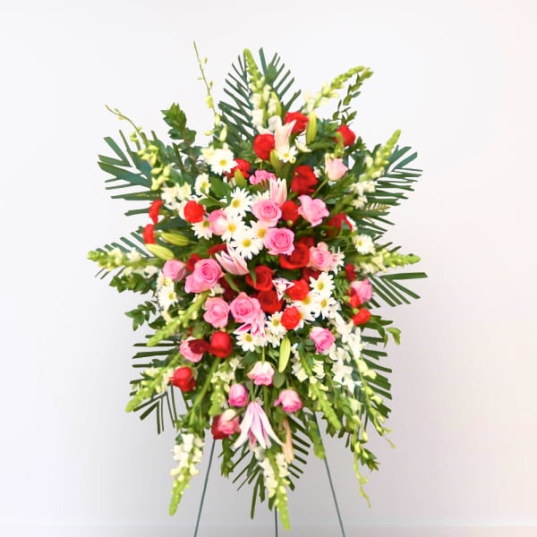 Standing floral spray with pink and red roses, white daisies, and tropical leaves