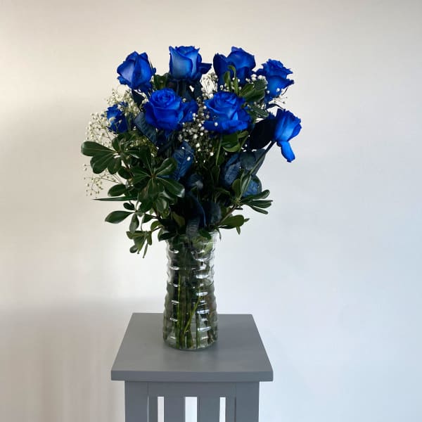 Blue roses in a clear glass vase with greenery