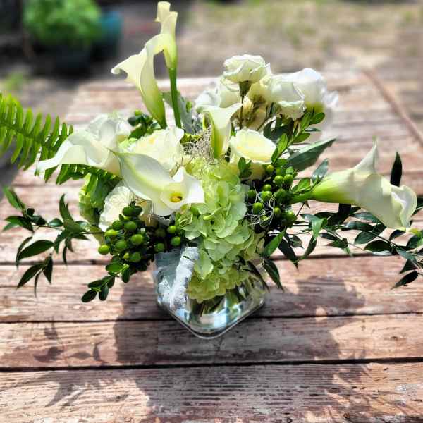 White calla lilies and roses in a glass vase with green accents